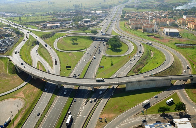 Vista aérea de um grande trevo com viadutos e rotatórias no Sistema Anhanguera-Bandeirantes, cercado por área urbana