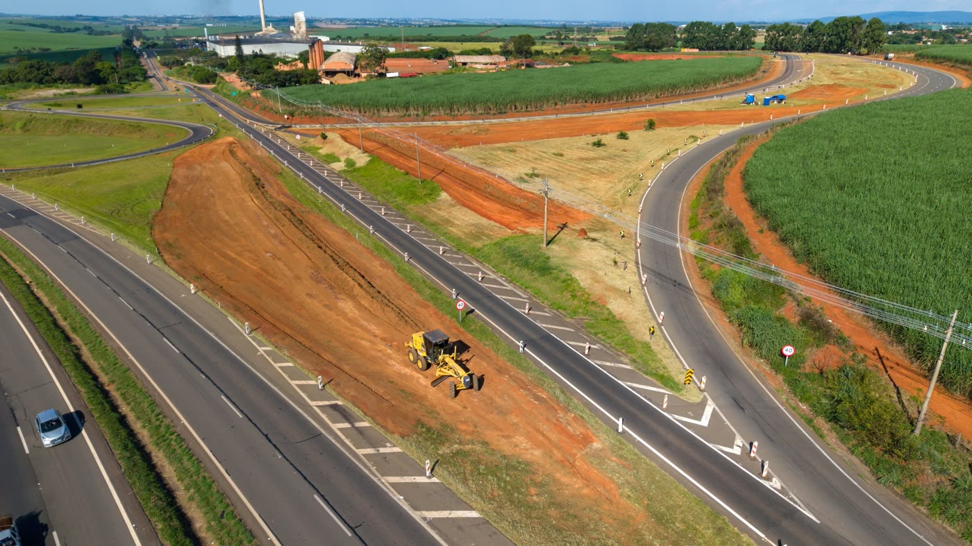Vista aérea de obras de implantação de via marginal, com terraplenagem em solo vermelho