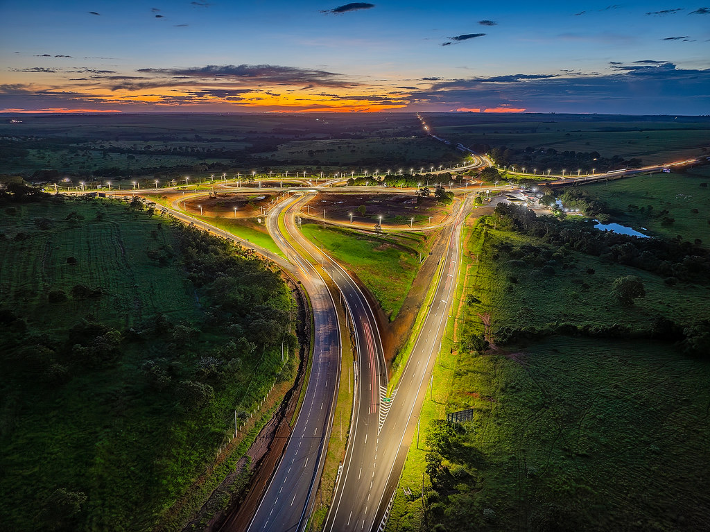 Vista aérea ao pôr do sol de trevo rodoviário com rastros de luz do tráfego, na concessão da Ecovias do Cerrado