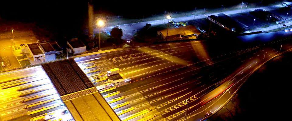 Vista aérea noturna de uma praça de pedágio no corredor Dom Pedro I, com rastros de luz do tráfego